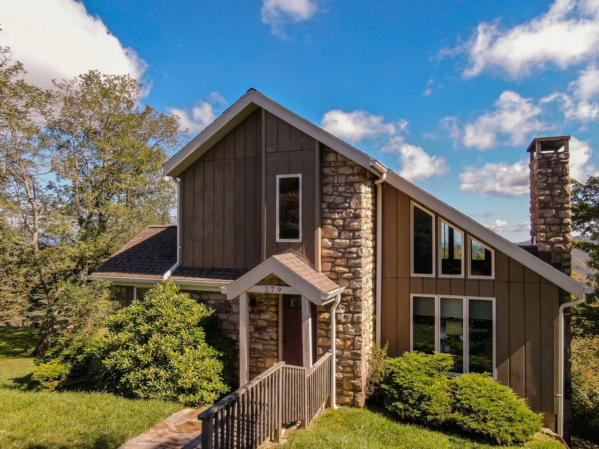 The image showcases the exterior of Aspen View, with its inviting stone façade, large windows that hint at scenic indoor-outdoor connections, wooden steps, and the surrounding lush greenery. The scene evokes an atmosphere of welcome and natural immersion, perfect for setting off on outdoor adventures or relaxing on the porch after a day of exploration.