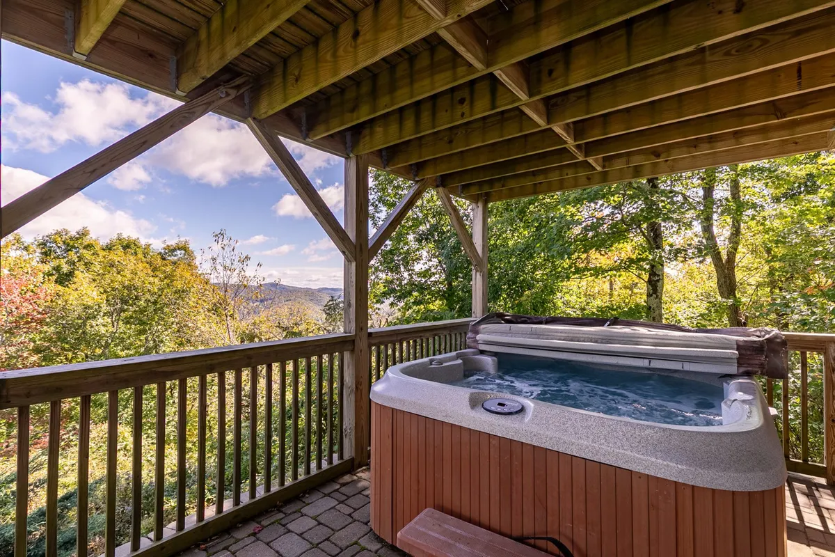A bubbling hot tub sits beneath a rustic wooden structure, overlooking scenic mountain views. The tranquil setting invites guests to unwind and soak while enjoying the outdoors, perfect for stargazing or watching the sunset.
