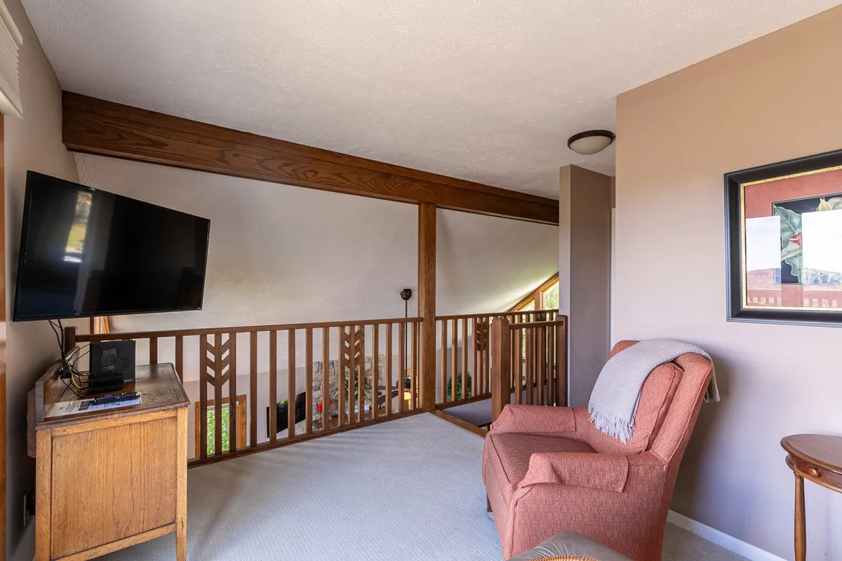 Cozy corner with a plush armchair, television, wooden railing, and framed artwork on the wall. The setup is ideal for unwinding after a day out, offering both relaxation and glimpses of personal style through curated decor.