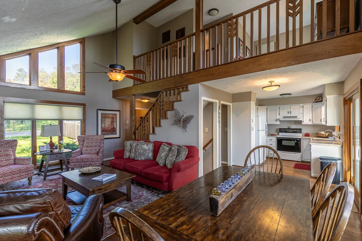 An inviting open-plan area with a red sofa, dining table, and visible staircase leading to another level, illuminated by generous natural light from large windows. The layout suggests multiple activity zones for families to gather, play games, or unwind after a day of outdoor fun.