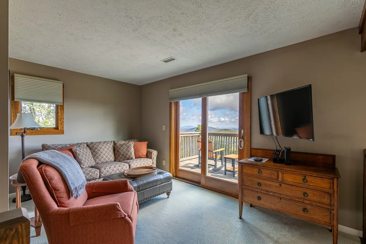 This interior features a sofa and armchair arranged around a TV and wooden side table, with a sliding door that opens to outdoor views. The setting suggests flexibility for both entertainment and quiet relaxation, offering a space that feels both intimate and connected to the outdoors.