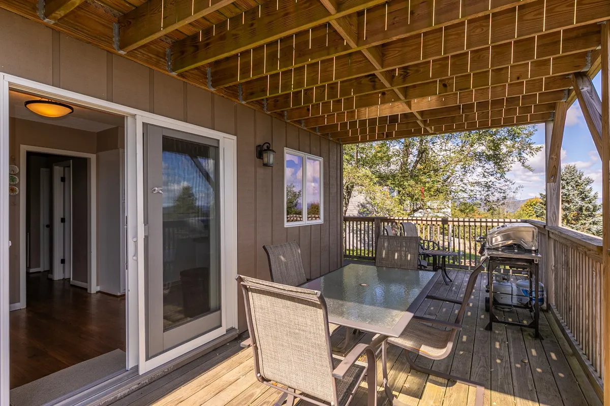 A spacious outdoor deck is featured, equipped with a dining table, grill, and expansive views of the surrounding landscape. The setup invites guests to enjoy outdoor meals, social gatherings, and the tranquility of the mountain environment. The deck is partially covered, offering shade and comfort for both people and pets.