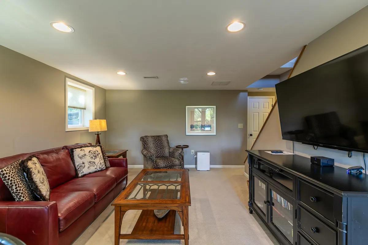 The image features a red leather sofa, wooden coffee table, large television, and a textured armchair arranged in a cozy, casual setting. The focal point is the big TV, with comfortable seating perfect for group activities like watching movies or playing games. The space exudes a relaxed, entertainment-focused atmosphere ideal for unwinding after a day outdoors.