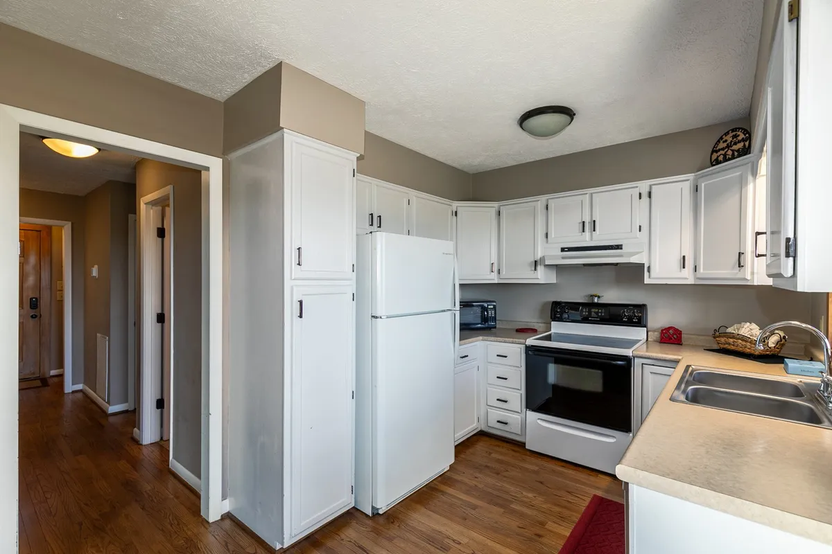 A view of the kitchen with white cabinetry, black appliances, and warm wooden flooring. The inviting design is ideal for meal prep and casual dining, while still connecting visually to the main living and dining spaces.