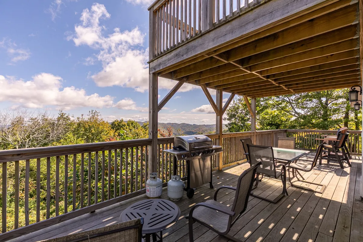 An exterior deck area featuring a grill, outdoor seating, and panoramic views of rolling hills and distant mountains. The relaxed atmosphere suggests opportunities for outdoor dining, socializing, and enjoying the scenery.