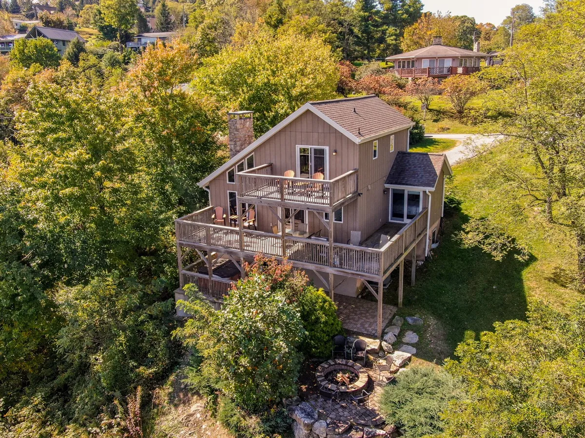 A wide view of the property’s main deck, featuring comfortable seating clustered around a crackling fire pit, all set against a backdrop of tall, serene trees. The inviting deck space is designed for gatherings, relaxation, and connection with nature.